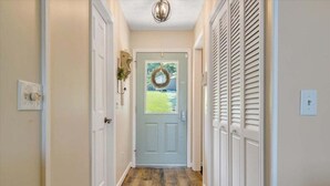 A hallway with a wooden floor, white walls, and a door at the end with a wreath. - Kelly Kove - Beach Area Sleeps 14, Private Dock, Pet Friendly (Penhook)