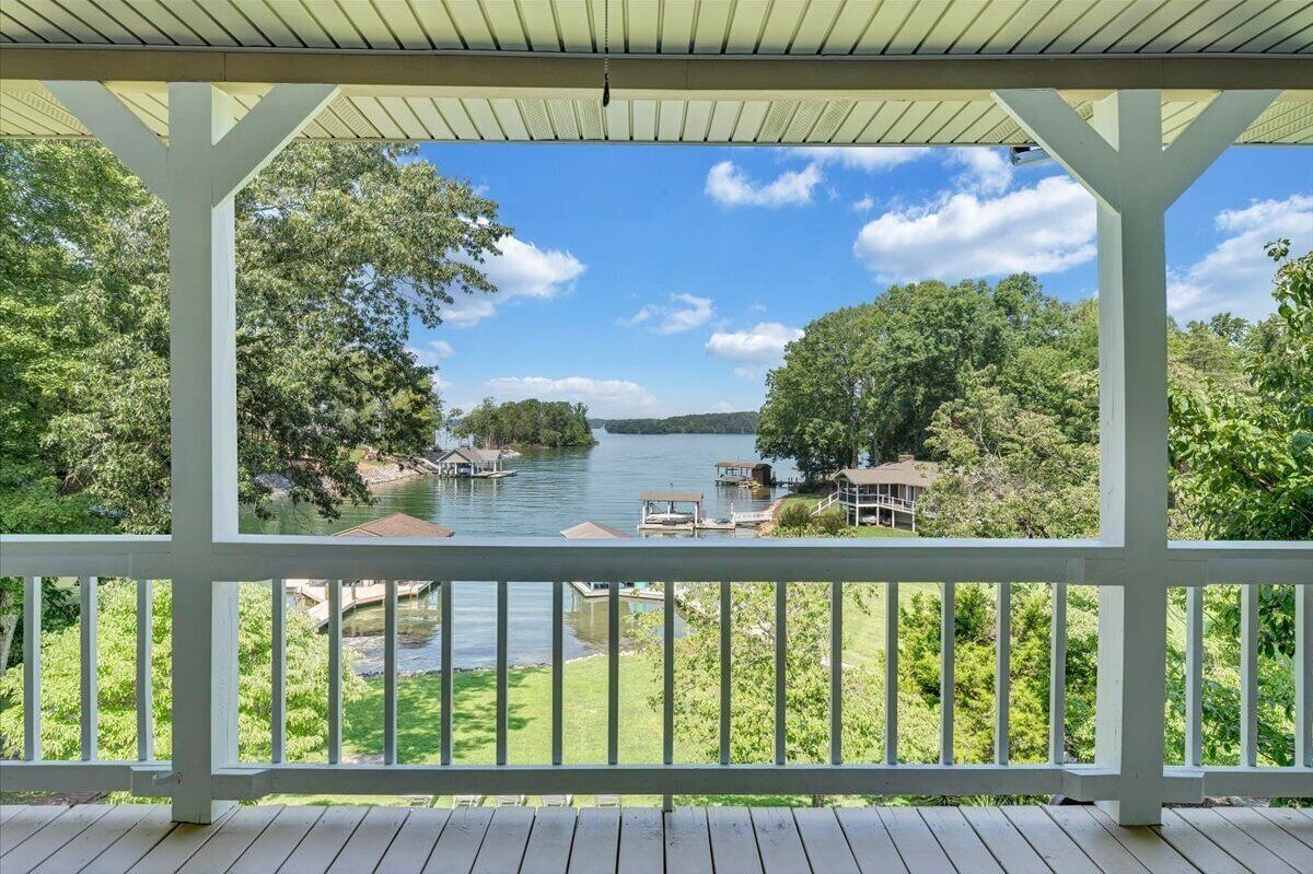 A covered deck with a view of a lake and surrounding greenery.