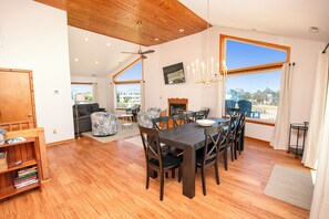 A dining area with a wooden table and chairs, a fireplace, and large windows offering a view. - Oceanside, Hot Tub, Close to Beach and Shopping! -  WW921, Sea 5 (Corolla)