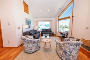 A spacious living room with a sofa set, a coffee table, and a view through a large window. - Oceanside, Hot Tub, Close to Beach and Shopping! -  WW921, Sea 5 (Corolla)