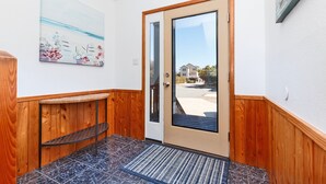 A hallway with a wooden door, a glass door, a small shelf, and a rug. - Oceanside, Close to Beach, Hot Tub- OS5H, Long Beach Day (Corolla)