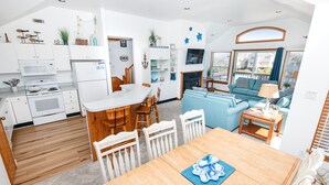 A modern kitchen with white cabinets, a microwave, and a stove. There is a dining area with a wooden table and chairs. - Oceanside, Close to Beach, Hot Tub- OS5H, Long Beach Day (Corolla)
