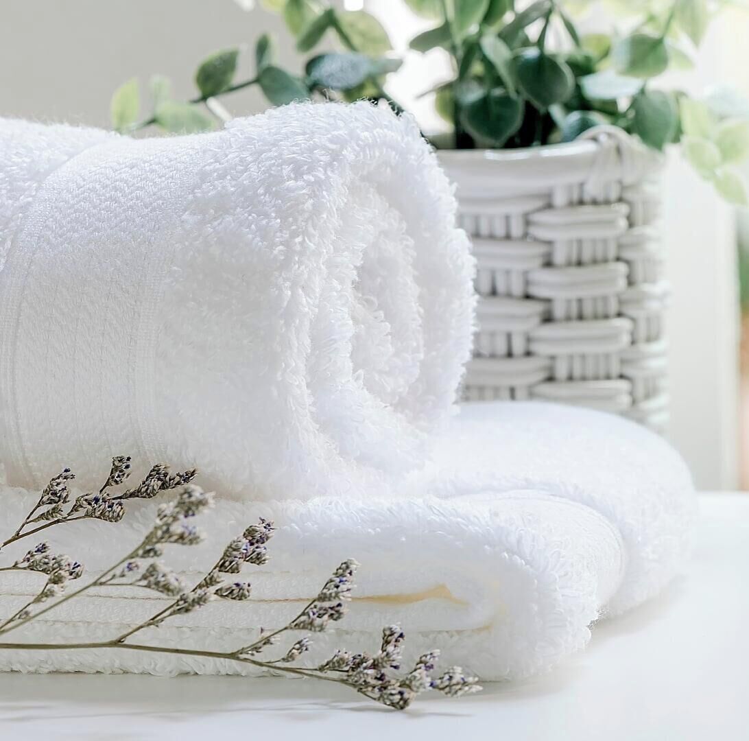 A neatly rolled white towel with a plant and dried flowers in the background.