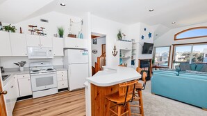 A modern kitchen with white cabinets, a wooden bar counter, and a blue sofa in the living area. - Oceanside, Close to Beach, Hot Tub- OS5H, Long Beach Day (Corolla)