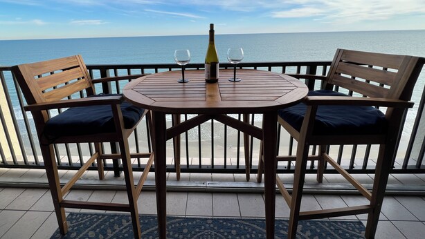 A wooden table with two chairs, a wine bottle, and two wine glasses on a balcony with a view of the sea. - WELCOME TO THE IVORY TOWER AT ARCADIAIN SHORES - 2 BEDROOM - CONDO ON THE OCEAN (Myrtle Beach)