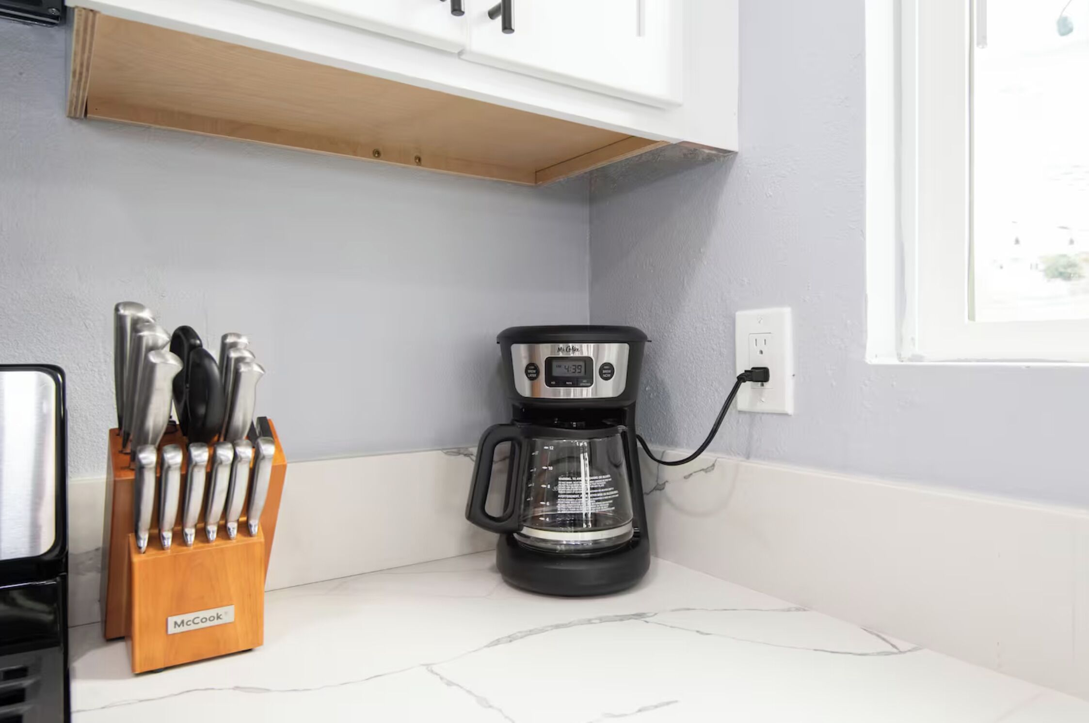 A kitchen with a coffee maker, a knife block, and a window.