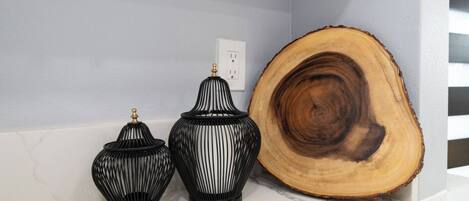 Three black vases with gold accents on a marble countertop, a large wooden slice, and a white electrical outlet on a light blue wall.