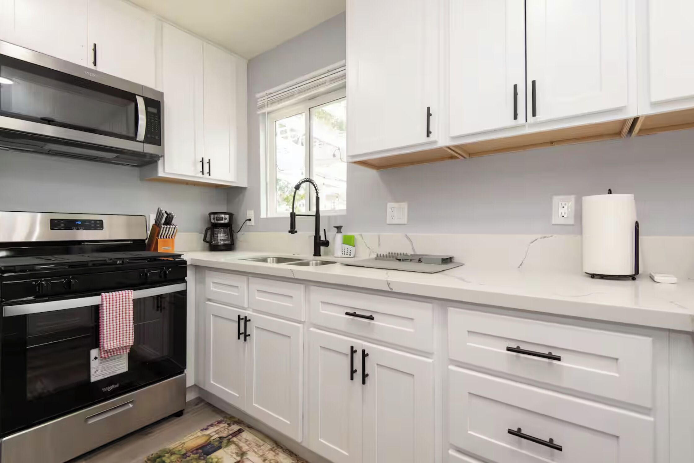 A modern kitchen with white cabinets, a stainless steel stove, a microwave, and a sink.