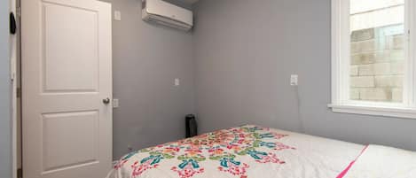 Un dormitorio con cama, ventana, unidad de aire acondicionado y puerta.