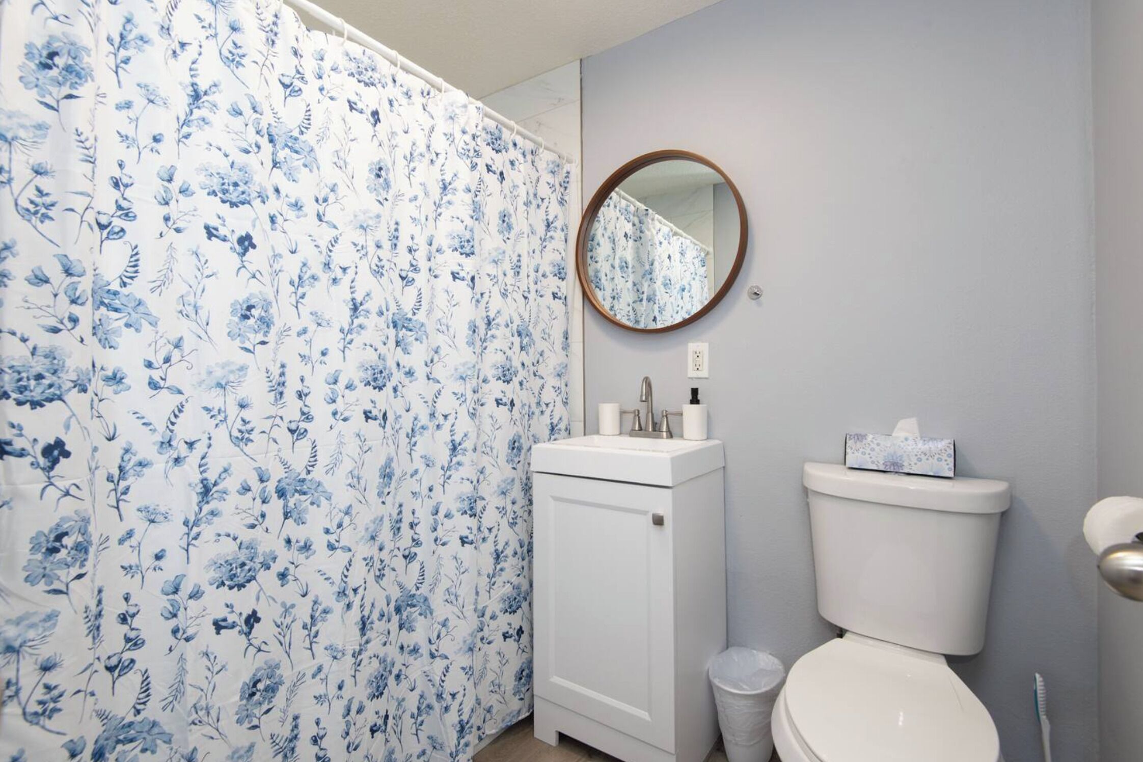 A bathroom with a floral shower curtain, a sink with toiletries, a toilet, and a mirror.