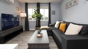 A modern living room with a flat-screen TV, a coffee table, a sofa, and a large window with curtains.