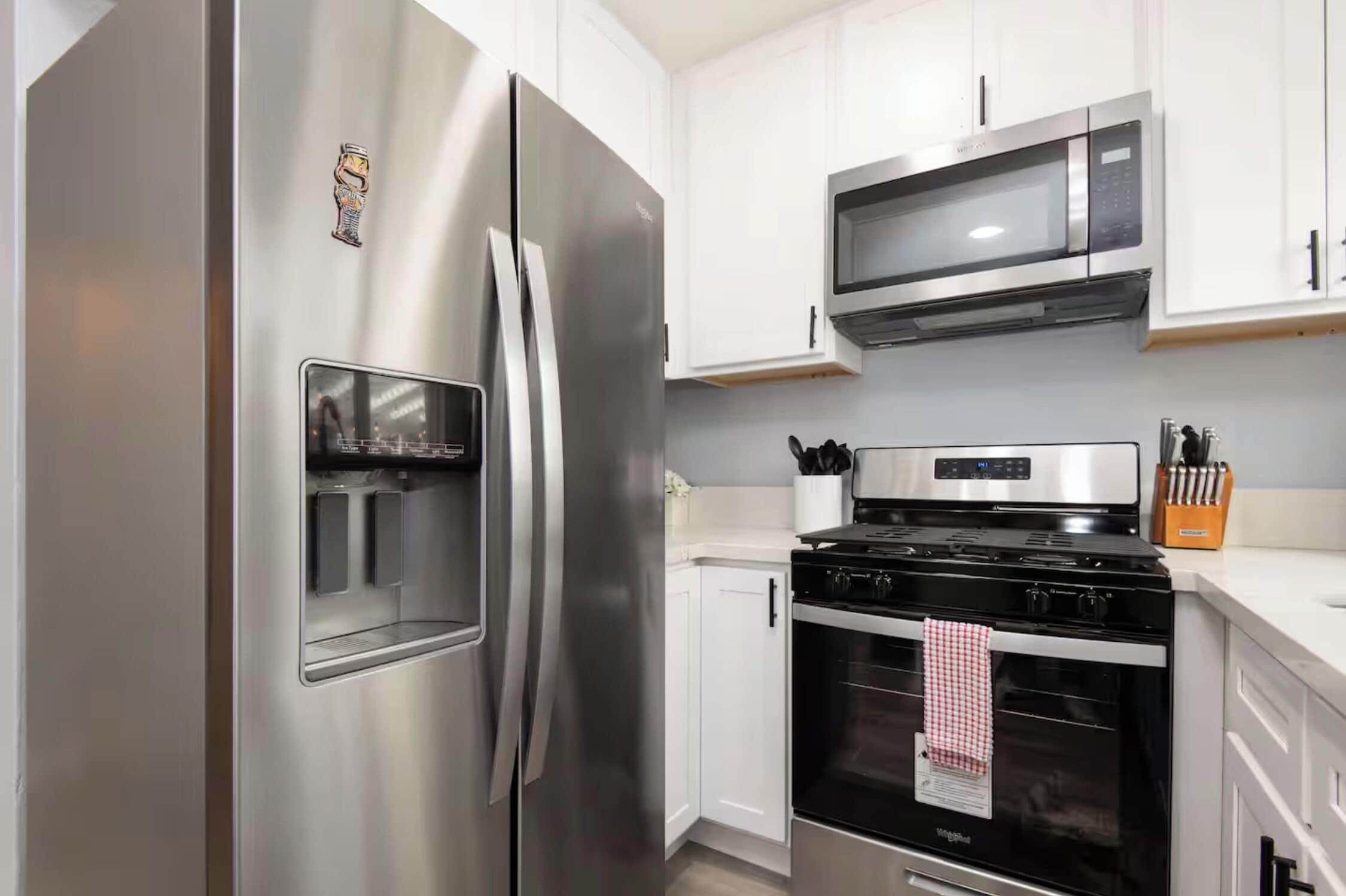 Una cucina moderna con elettrodomestici in acciaio inossidabile, mobili bianchi, un forno a microonde e un piano cottura.