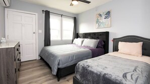 A bedroom with two beds, a ceiling fan, a window with curtains, and a wall-mounted artwork.
