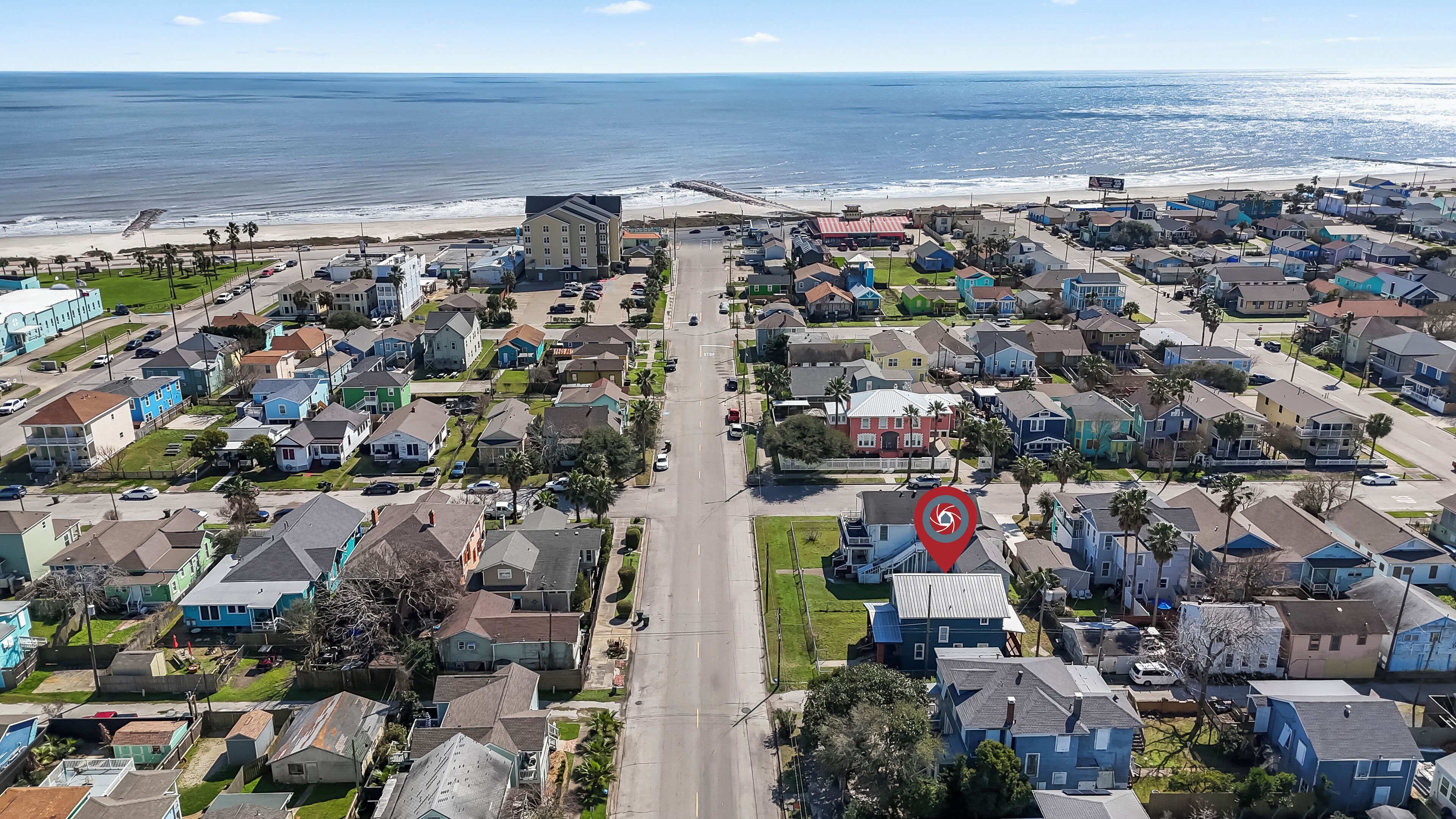 An aerial view of a coastal residential area with houses, a beach, and a clear sky.