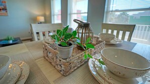 A dining area with a table set for two, featuring a woven placemat, a potted plant, a candle holder, and matching dinnerware.