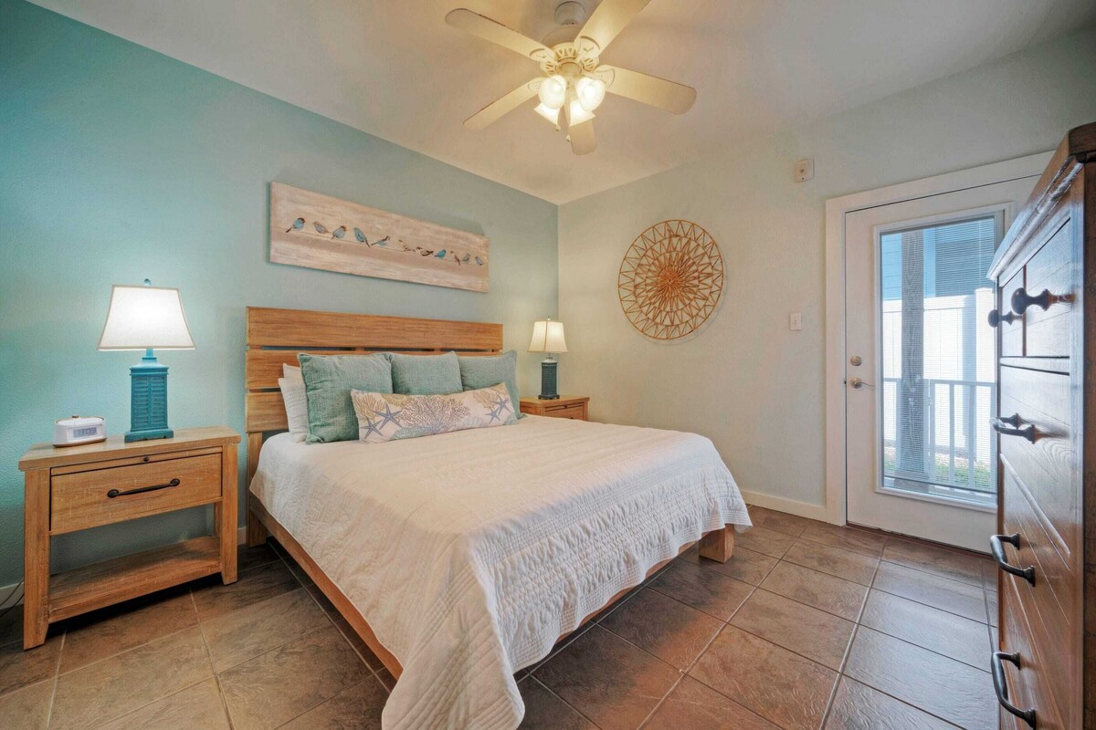 A bedroom with a bed, two nightstands, a ceiling fan, a window, and a door.