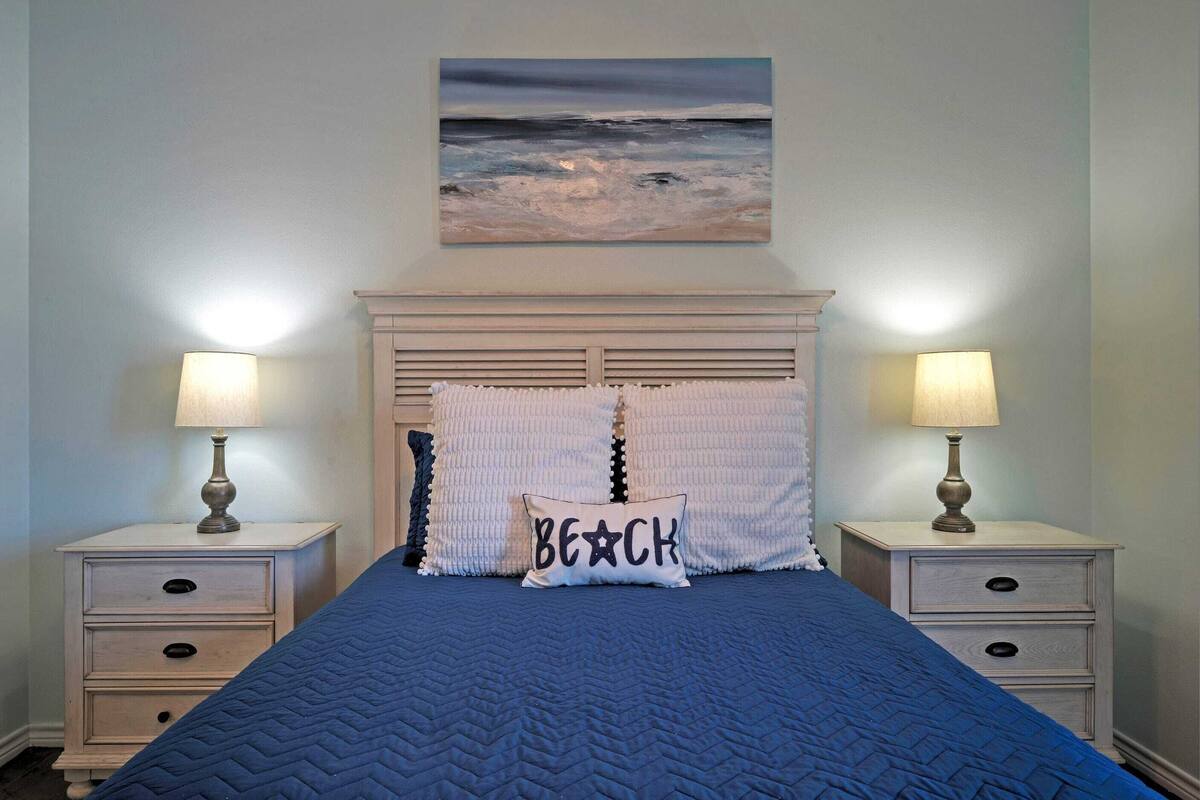 Un dormitorio con una cama, dos mesitas de noche, un cabecero y un cuadro de una escena de playa.