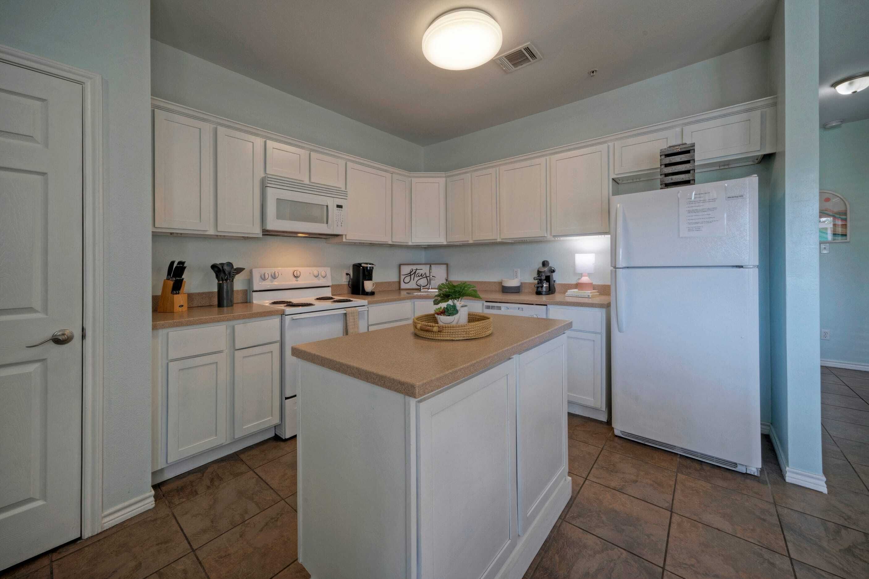 A kitchen with white cabinets, a central island, a microwave, a refrigerator, and a sink.