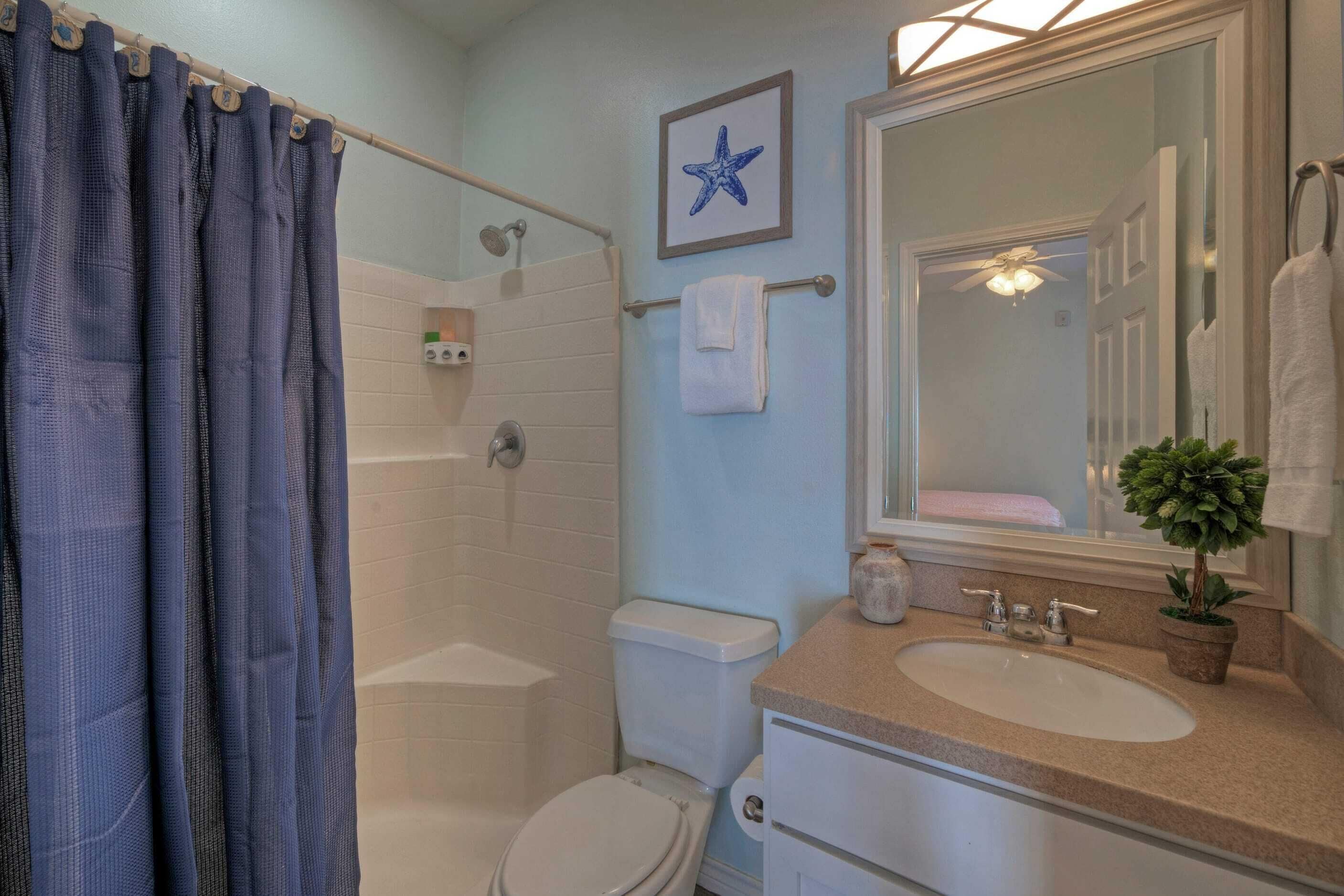 A bathroom with a shower, toilet, sink, and a starfish decoration on the wall.