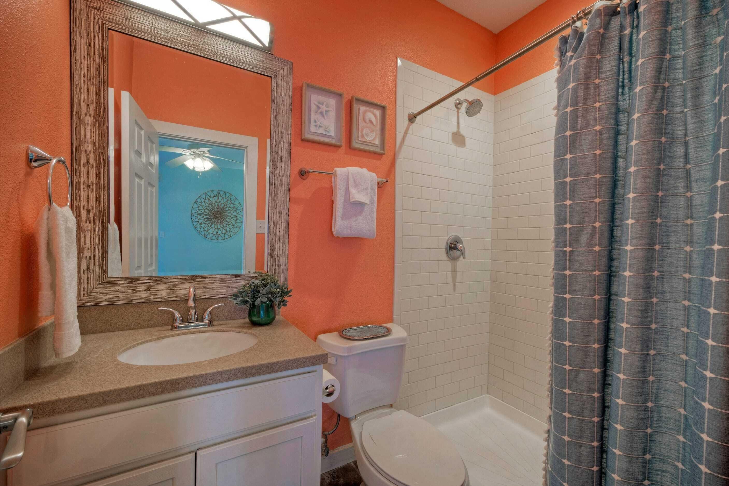 A bathroom with a white sink, a toilet, a shower with a curtain, and a mirror with a towel hanging on the wall.