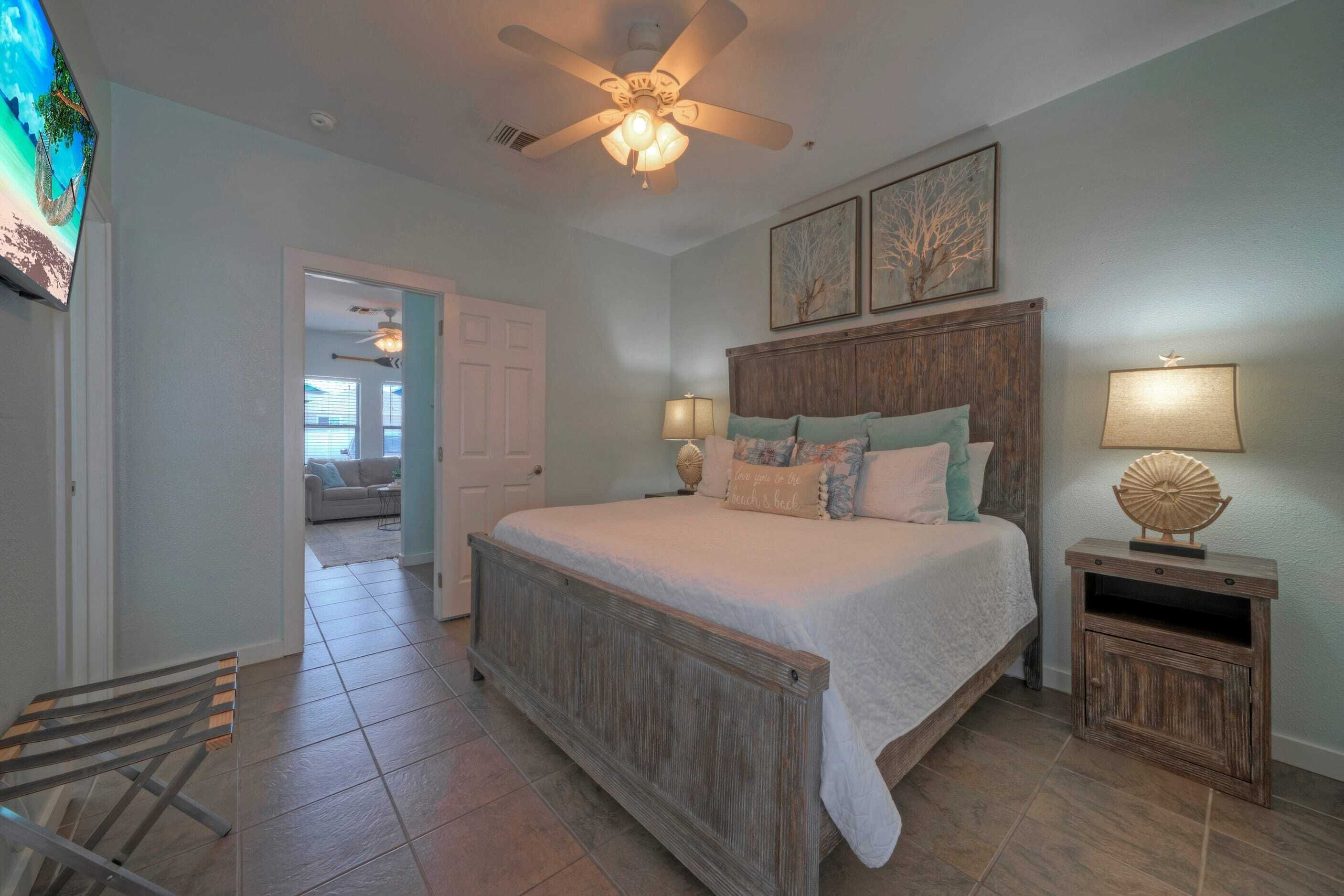 A bedroom with a wooden bed, two bedside lamps, a ceiling fan, and a TV mounted on the wall.