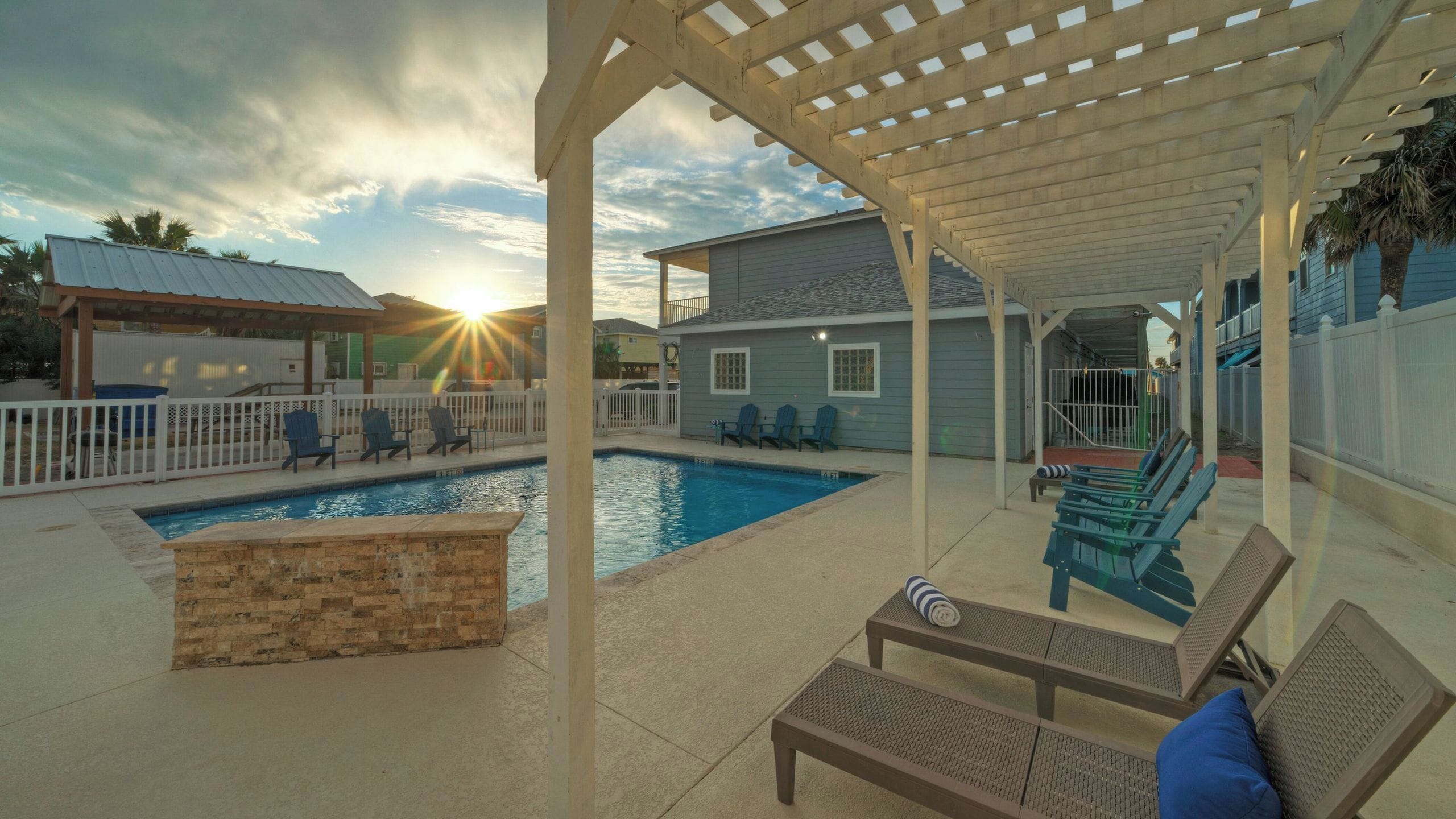 A covered outdoor swimming pool area with lounge chairs and a pergola.