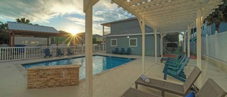 A covered outdoor swimming pool area with lounge chairs and a pergola.