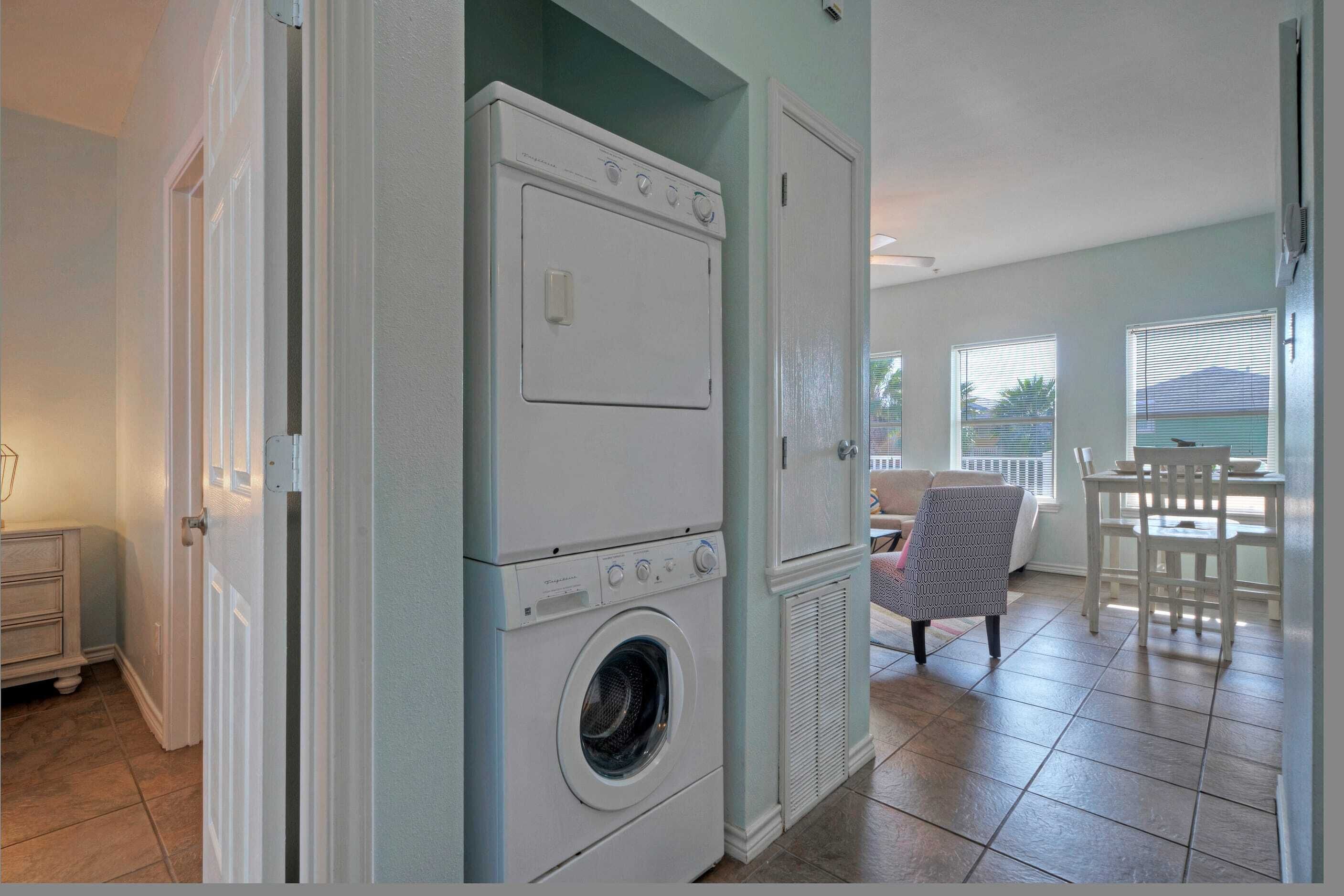 A laundry room with stacked washers and dryers, a dining area with a table and chairs, and a view of the outdoors through a window.