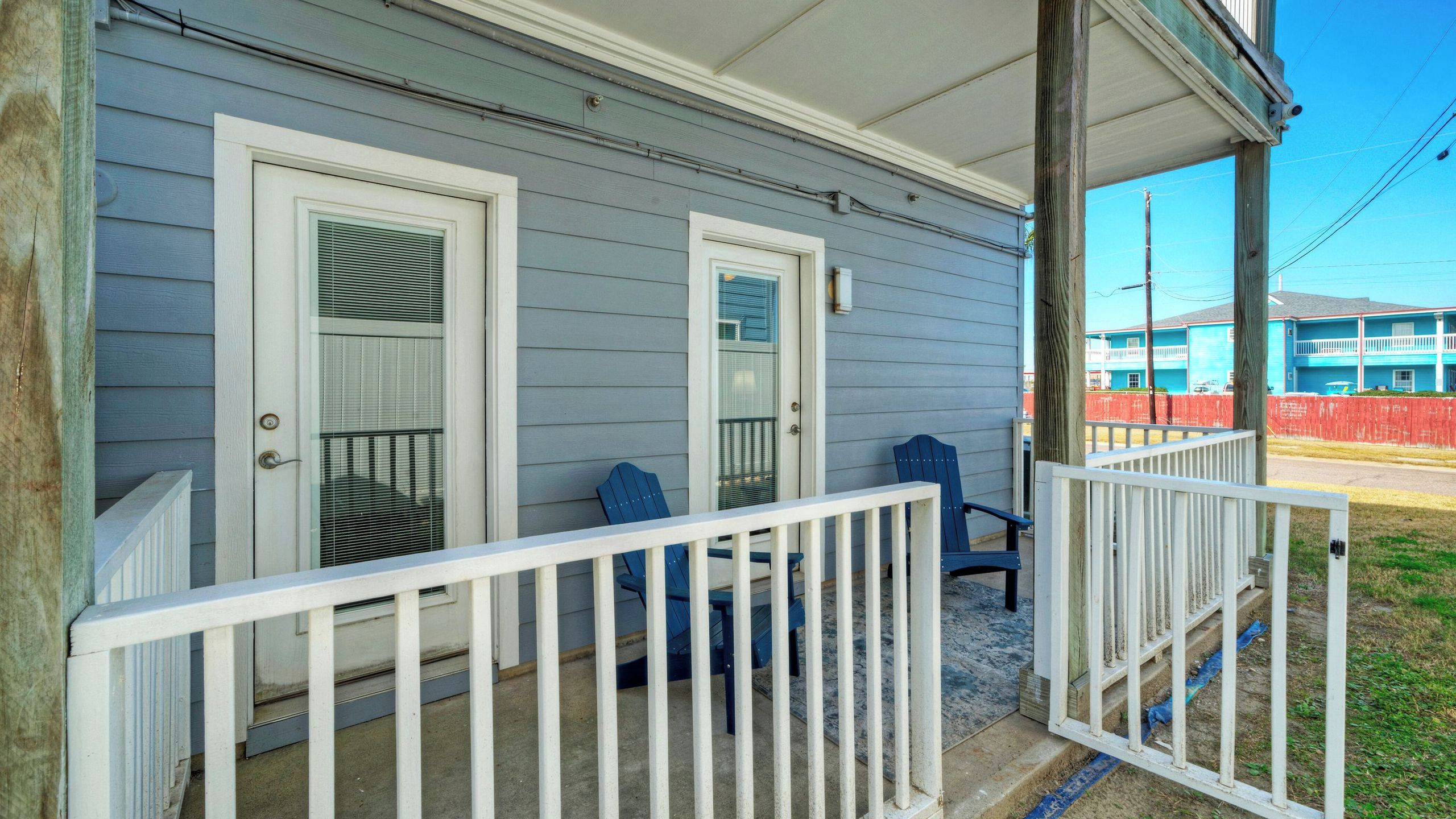 A porch with two doors, a railing, and two chairs.