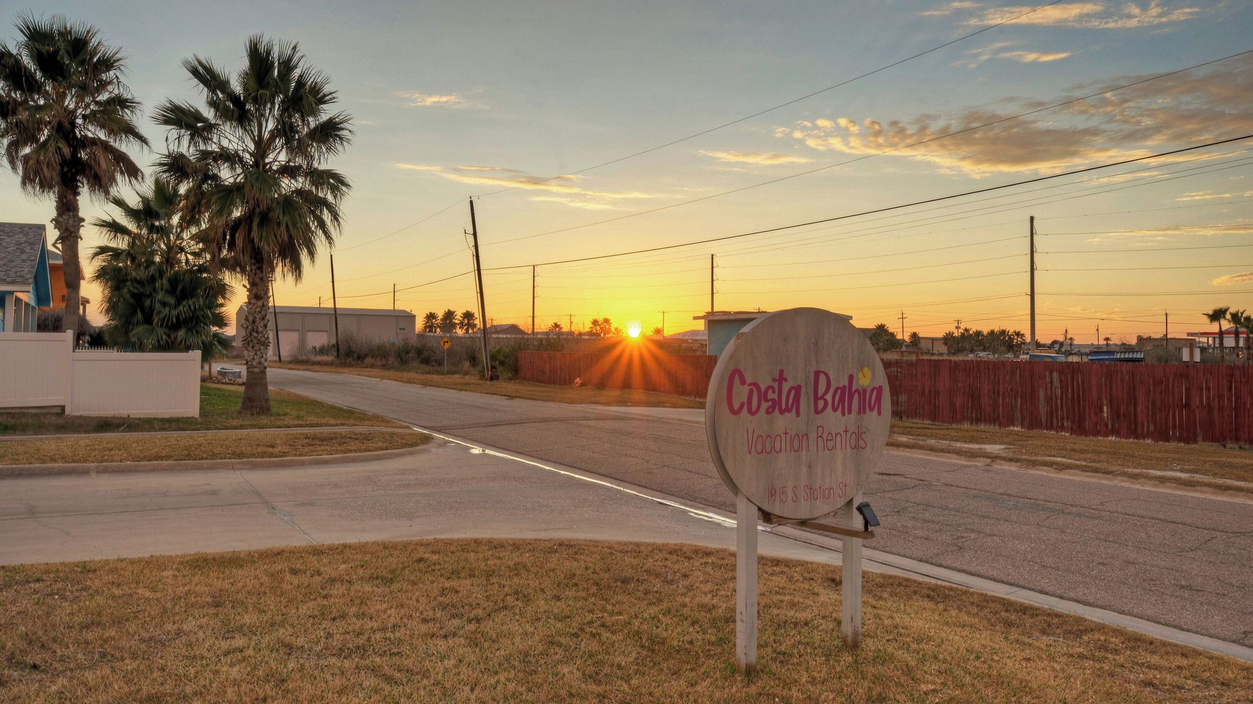 A sign for Costa Bahia Vacation Rentals with a sunset in the background.