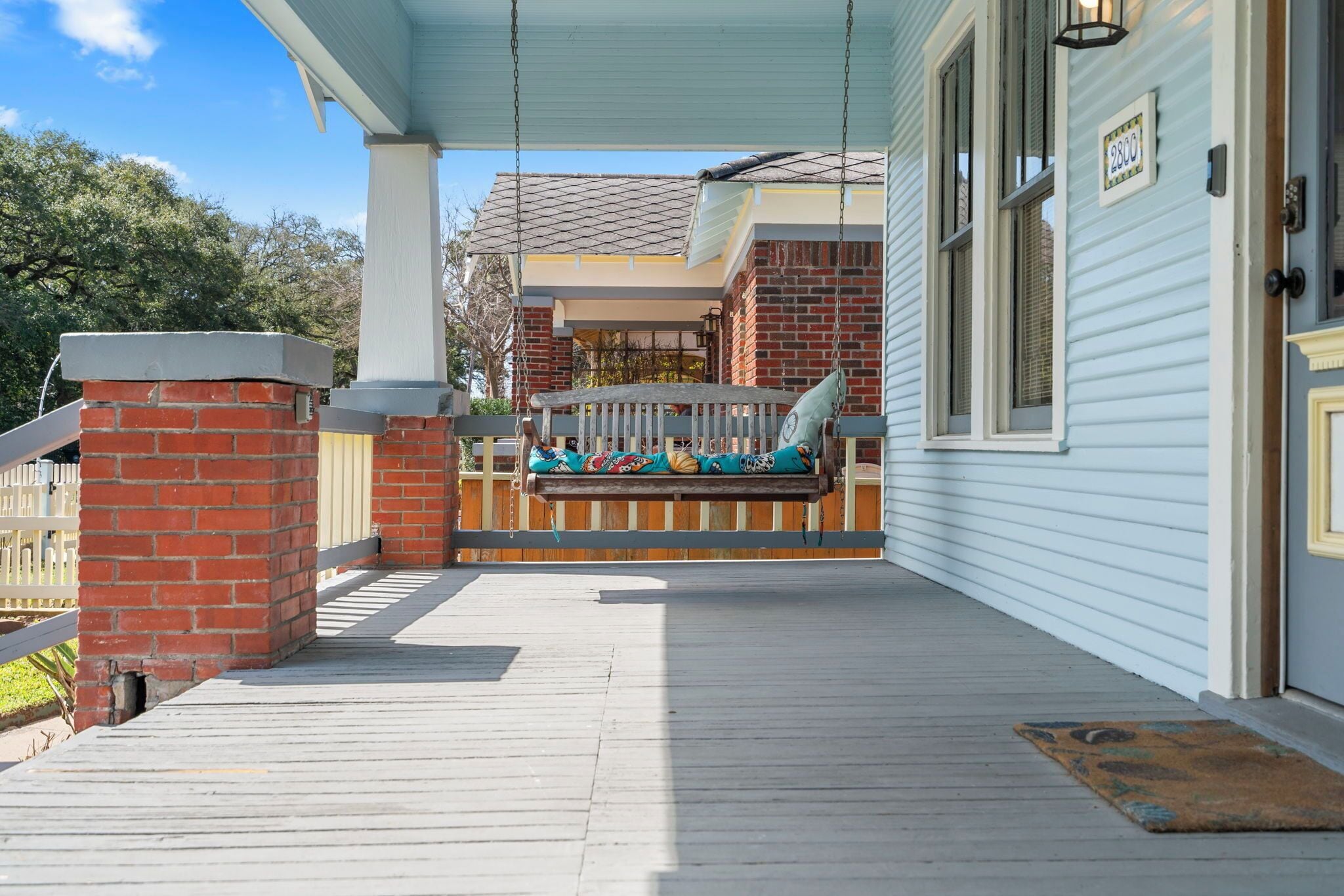 A porch with a swing, a brick pillar, and a wooden deck.
