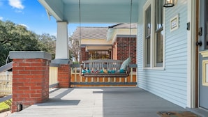A porch with a swing, a brick pillar, and a wooden deck.