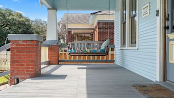 A porch with a swing, a brick pillar, and a wooden deck.