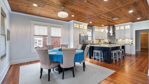 A spacious kitchen with wooden ceiling beams, a central island with stools, and a dining area with a round table and chairs.