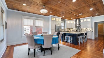 A spacious kitchen with wooden ceiling beams, a central island with stools, and a dining area with a round table and chairs.