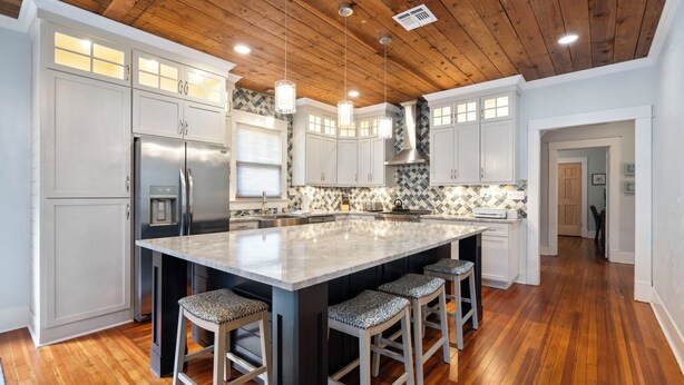 A spacious kitchen with a large island, wooden ceiling, and white cabinetry.