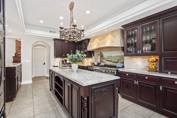 A spacious kitchen with dark wood cabinets, a large island, and a stone fireplace.