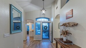 A spacious hallway with wooden flooring, a wooden bench, a mirror, and a decorative wall piece.