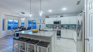 A modern kitchen with white cabinets, a large island with bar stools, stainless steel appliances, and pendant lighting.