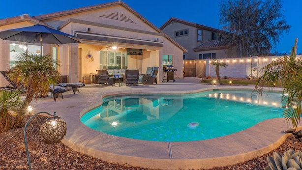 A residential property with a swimming pool, outdoor seating, and a covered patio area.