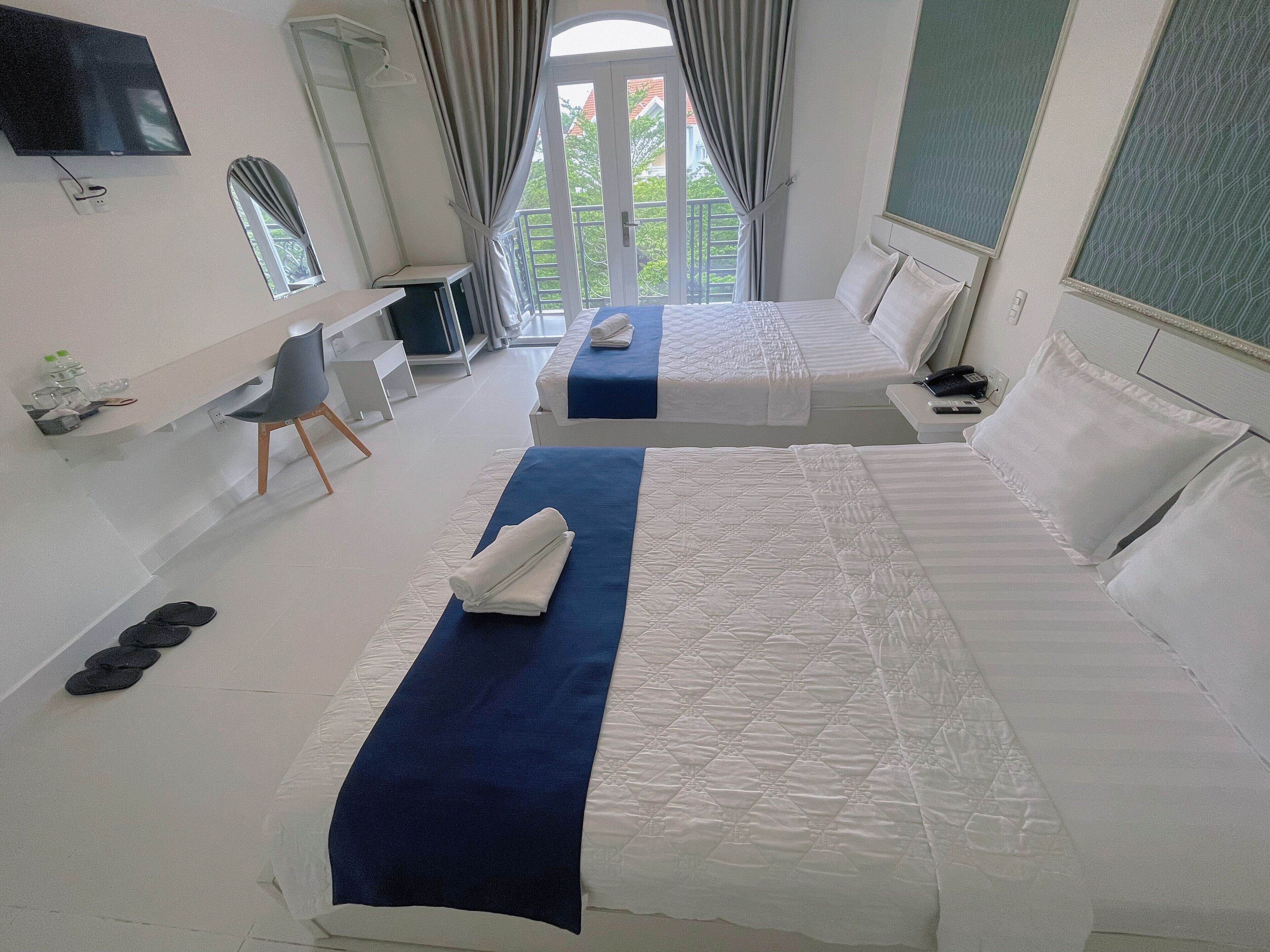 A hotel room with two beds, a desk, a chair, and a TV.