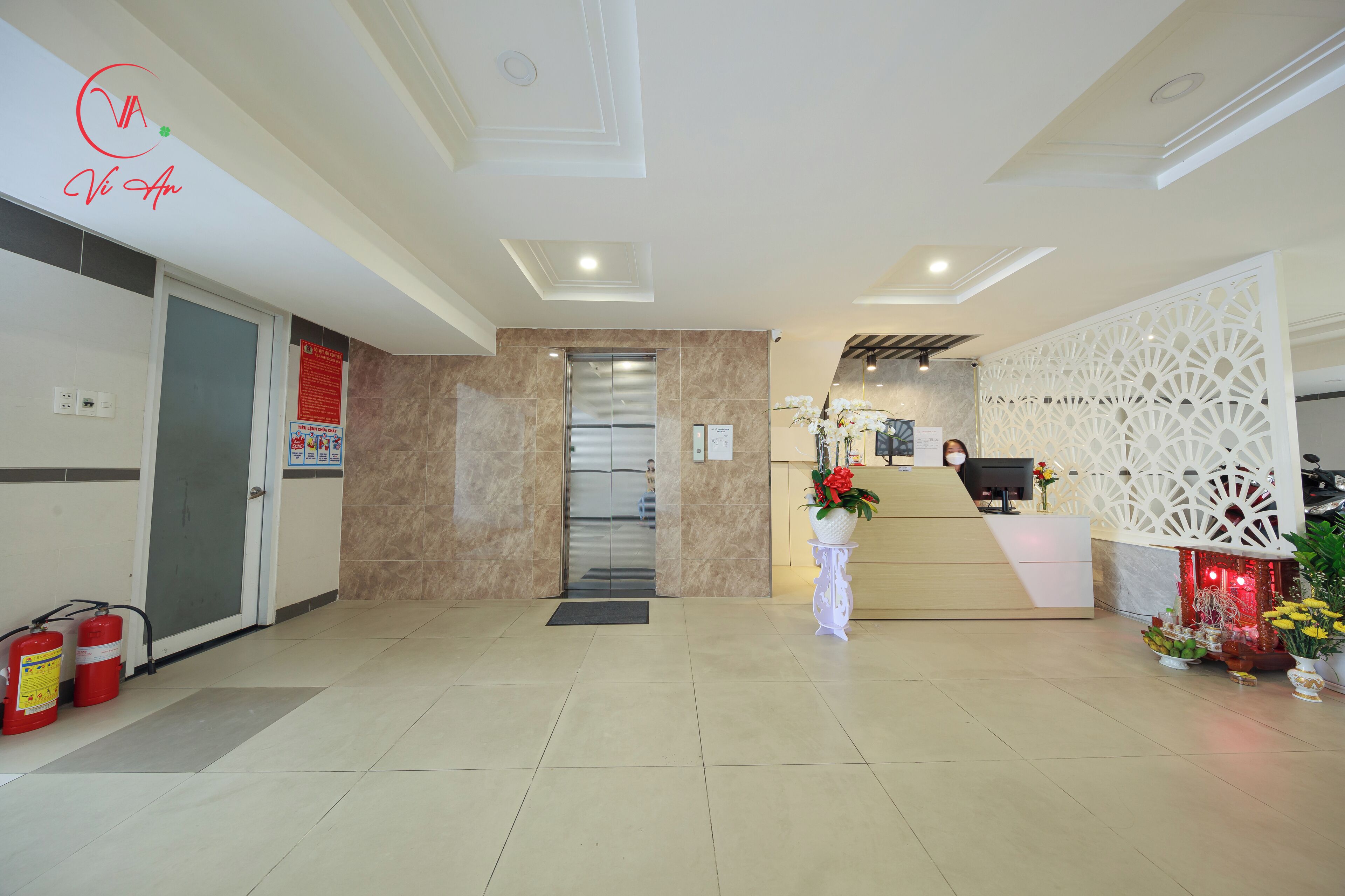 A hotel reception area with a reception desk, a glass elevator, and a decorative white partition.