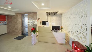 Zona de recepción con mostrador, televisor y un panel decorativo blanco.