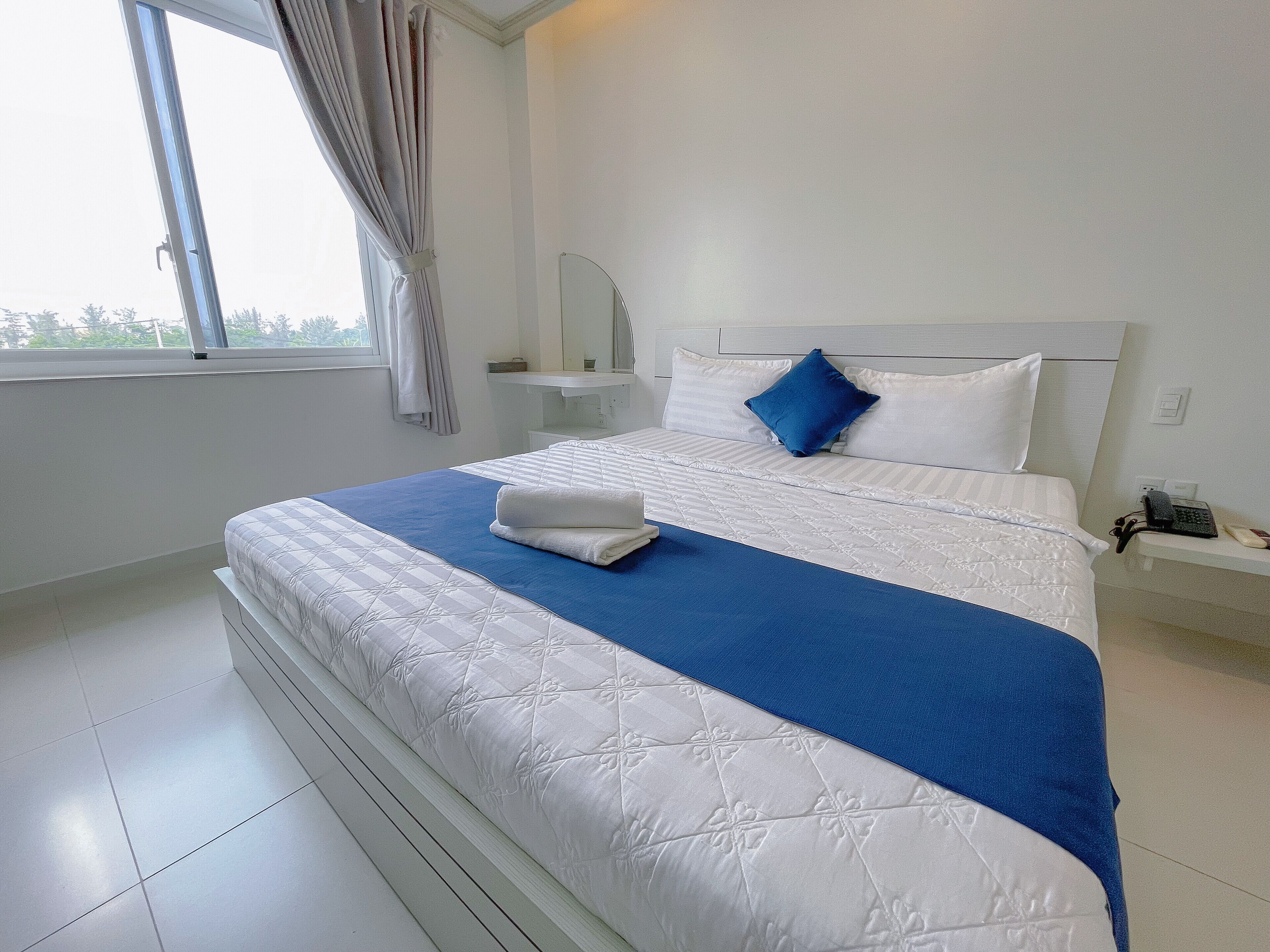 A neatly made bed with a blue and white bedspread, a white headboard, and a bedside table with a telephone.