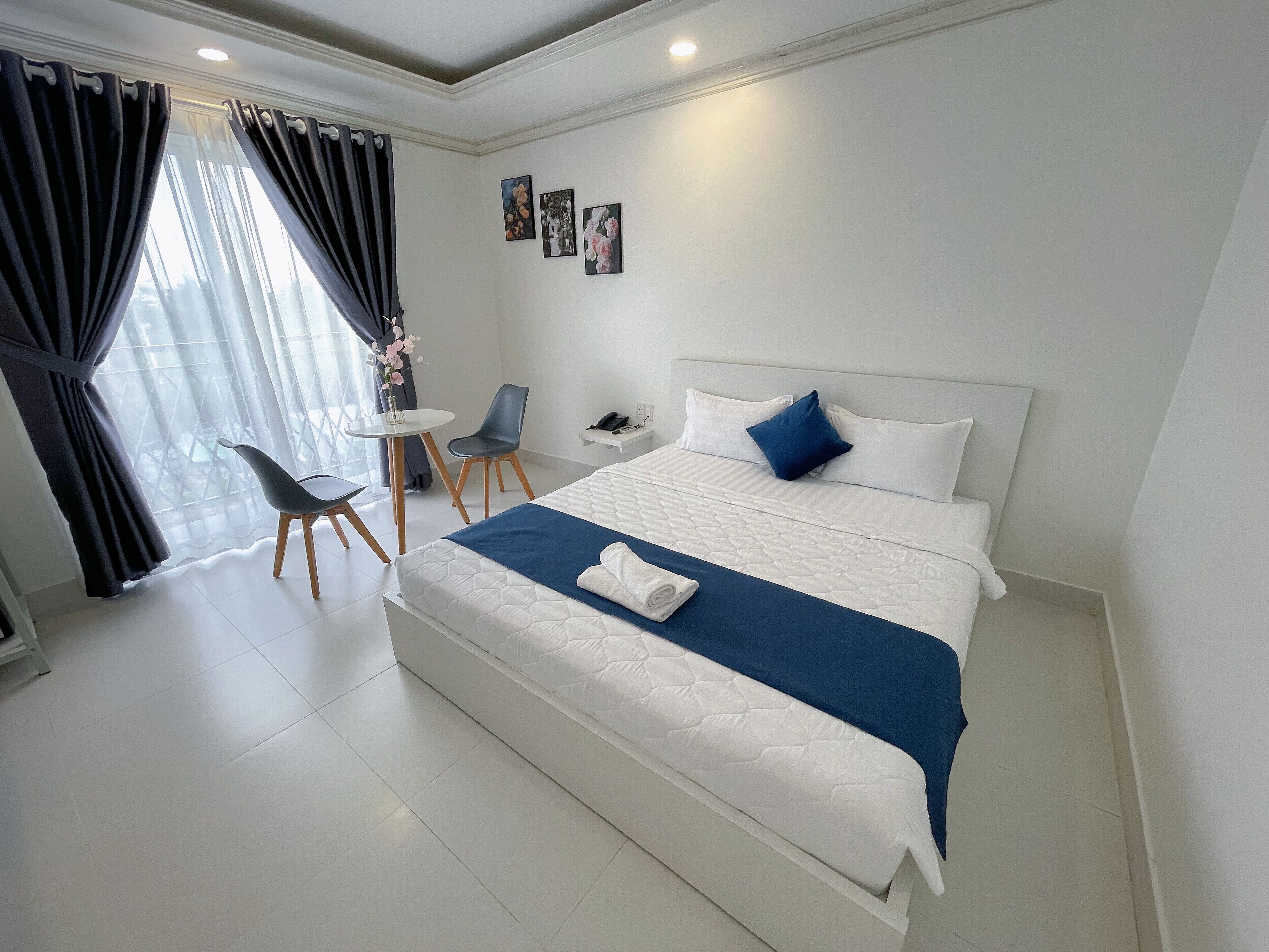A hotel room with a large bed, a small table, two chairs, and a window with curtains.