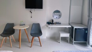 Una habitación de hotel pequeña y moderna con una cama, un escritorio con silla, un televisor montado en la pared, un refrigerador pequeño y una zona de ducha.