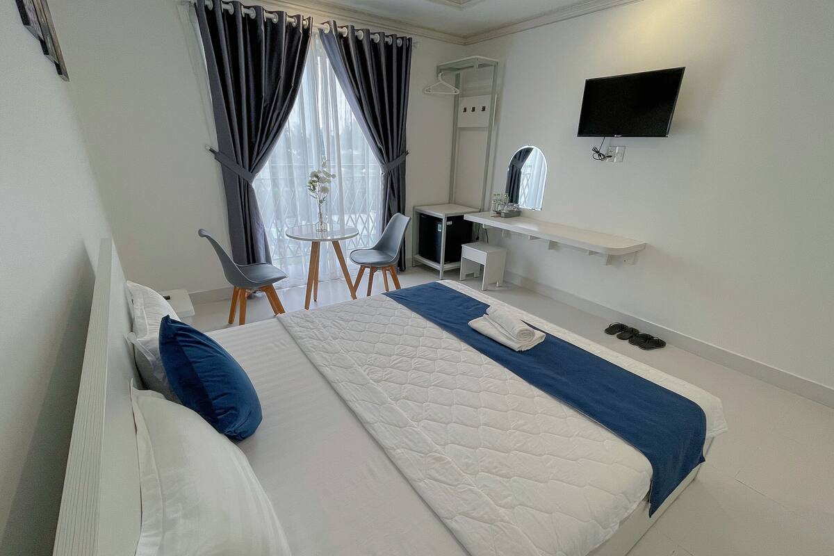 A hotel room with a bed, a desk, a chair, a TV, and a window with curtains.
