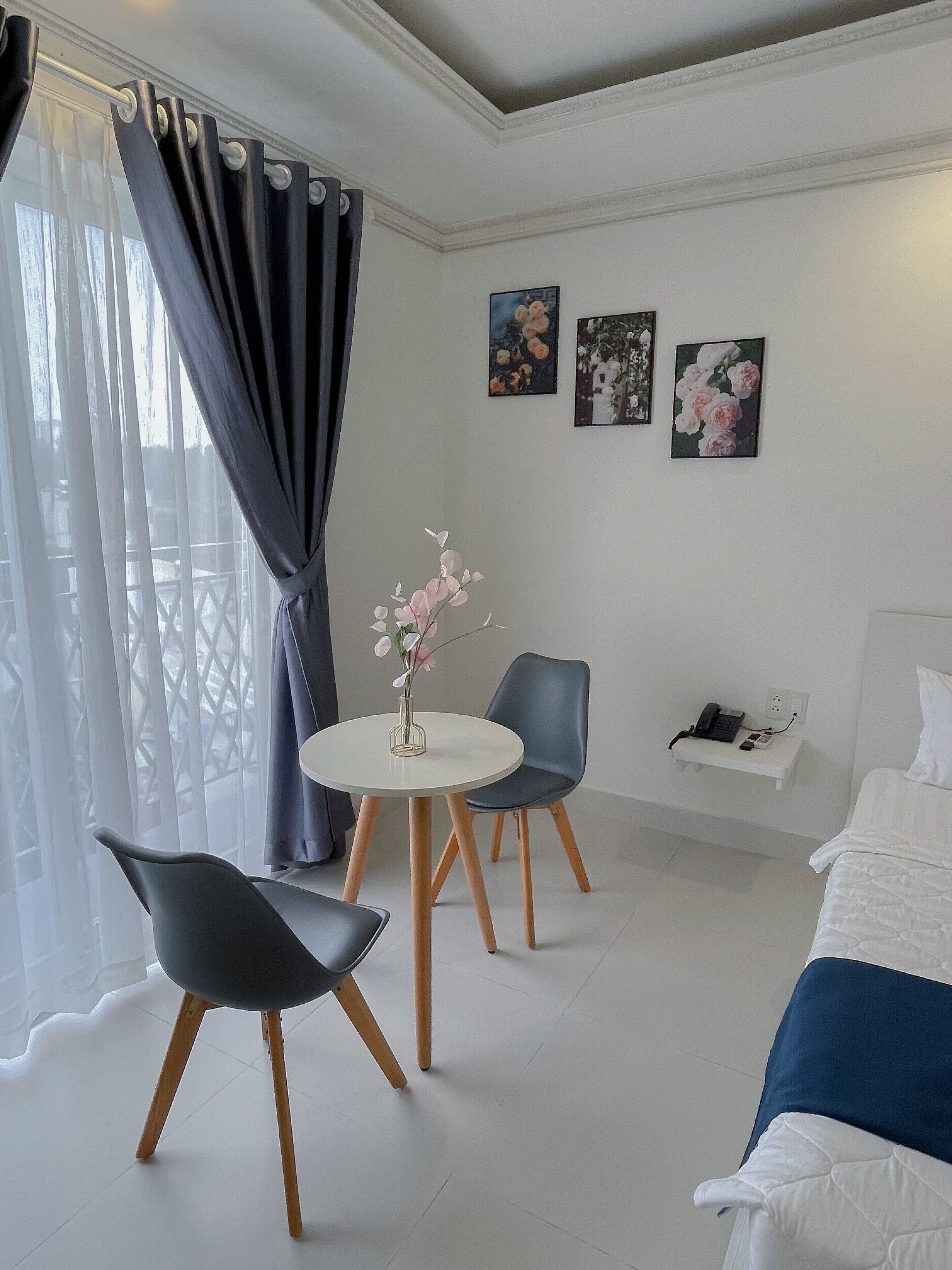 A modern hotel room with a bed, a round table with chairs, a vase with flowers, and artwork on the wall.