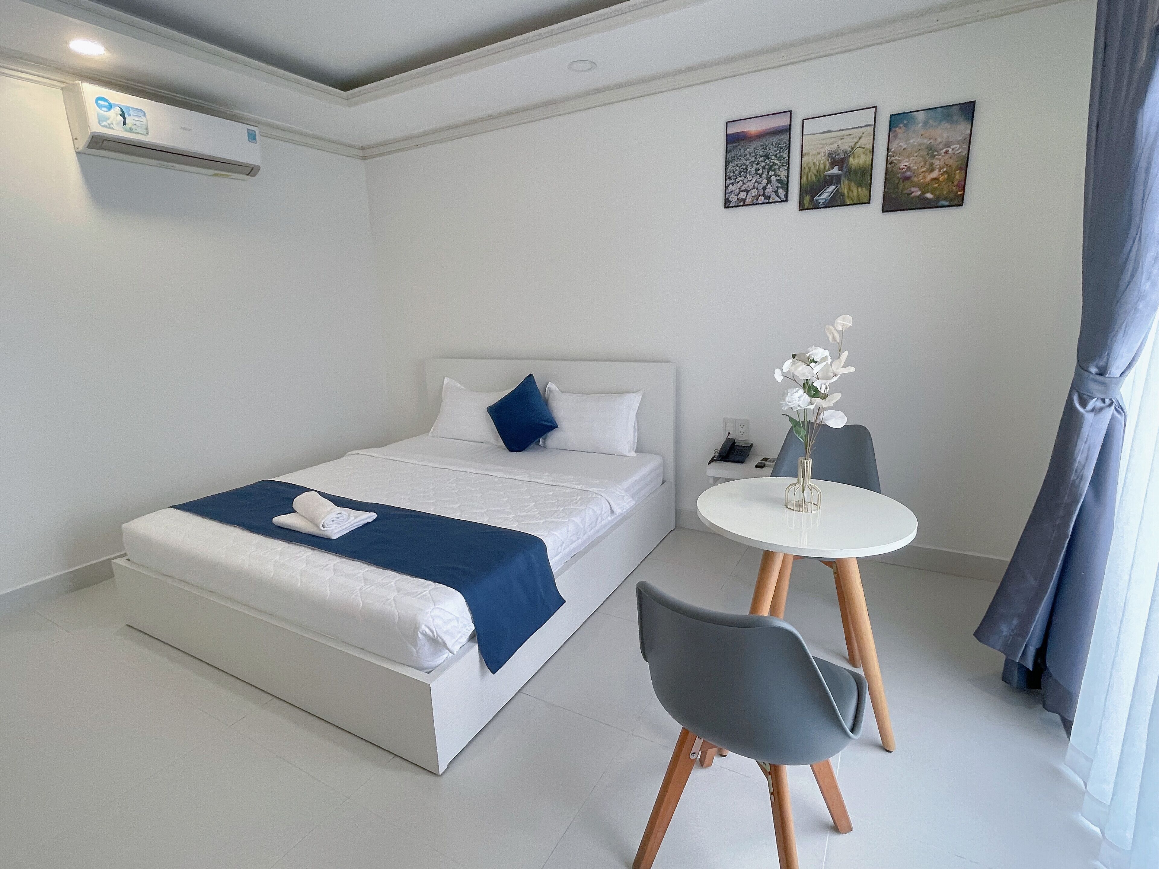 A modern hotel room with a neatly made bed, a small round table with a vase of flowers, and a chair.