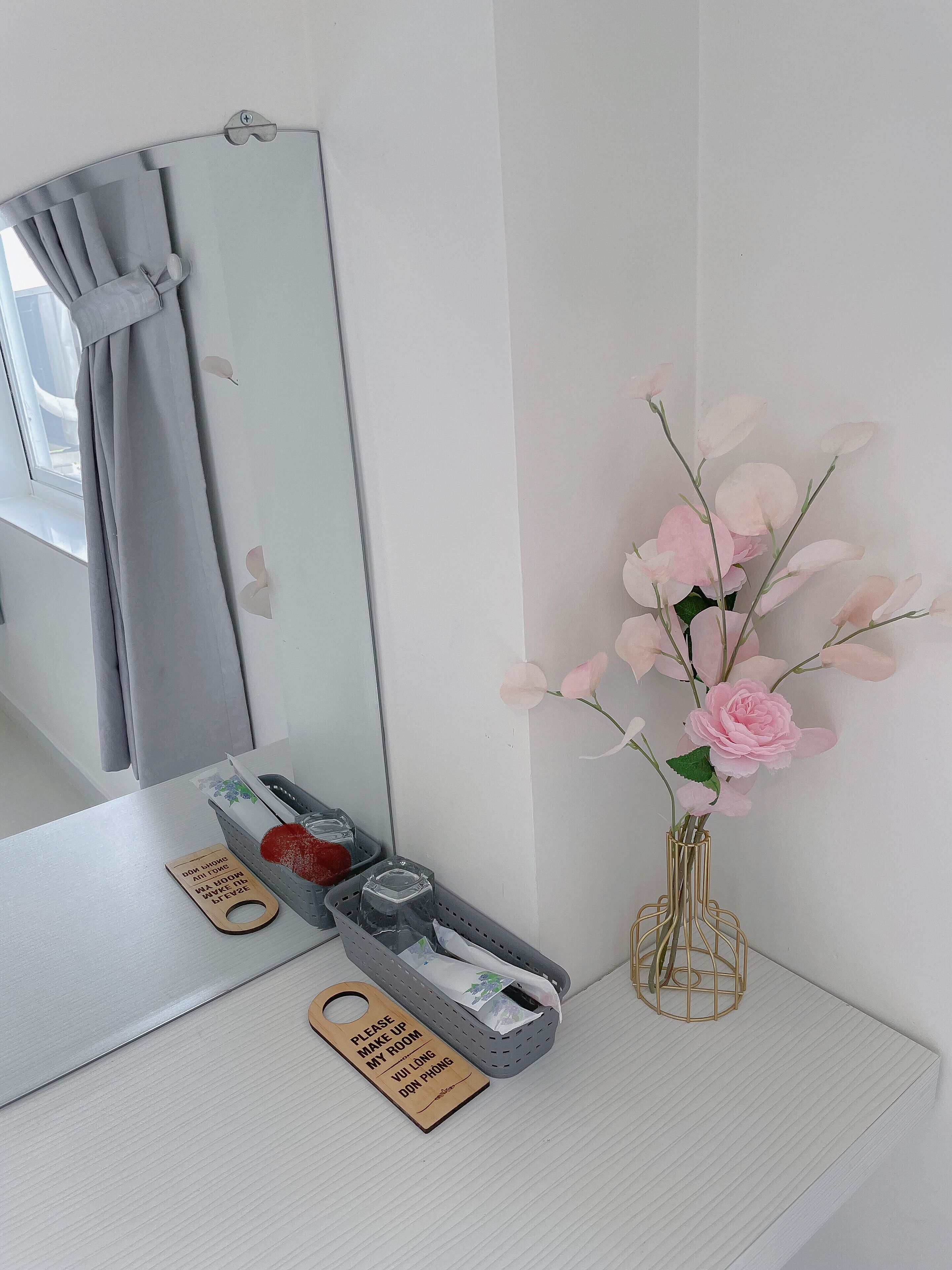 A bathroom vanity with a mirror, a tissue box, a hand soap dispenser, and a vase with pink flowers.